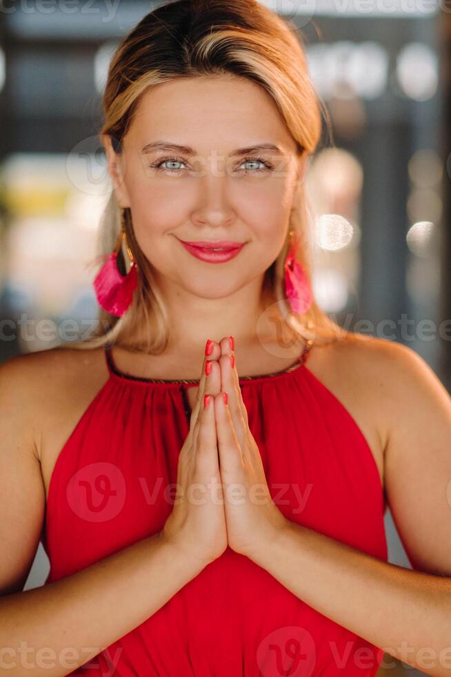 Portrait of a smiling girl in a red dress stands in the interior with her hands clasped in front of her photo