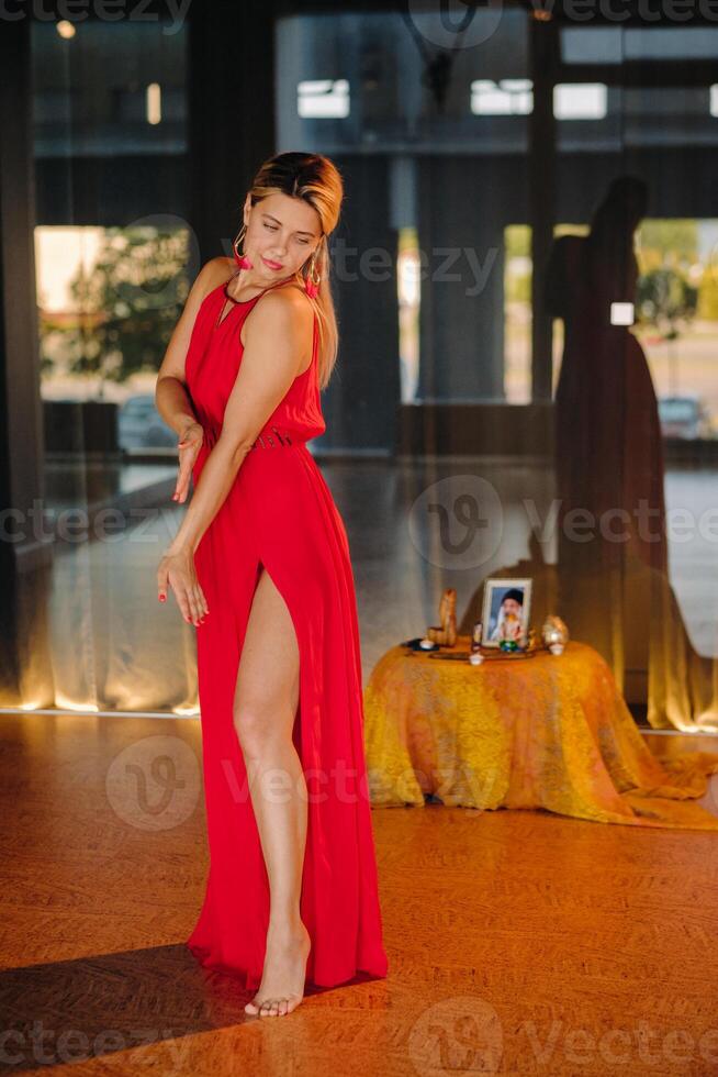 A girl in a red dress moves in a dance meditating indoors . Dynamic dance photo