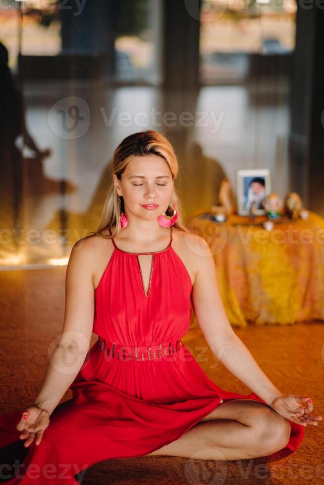 Meditation and concentration. a woman in a red dress, sitting on the floor with her eyes closed, is practicing medicine indoors. Peace and relaxation photo