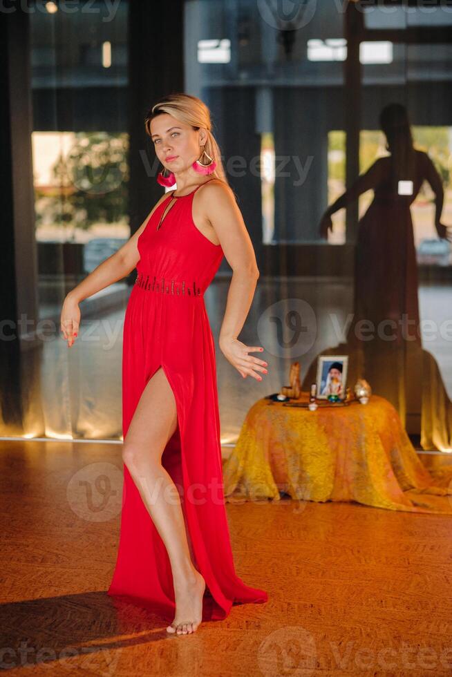 A girl in a red dress moves in a dance meditating indoors . Dynamic dance photo