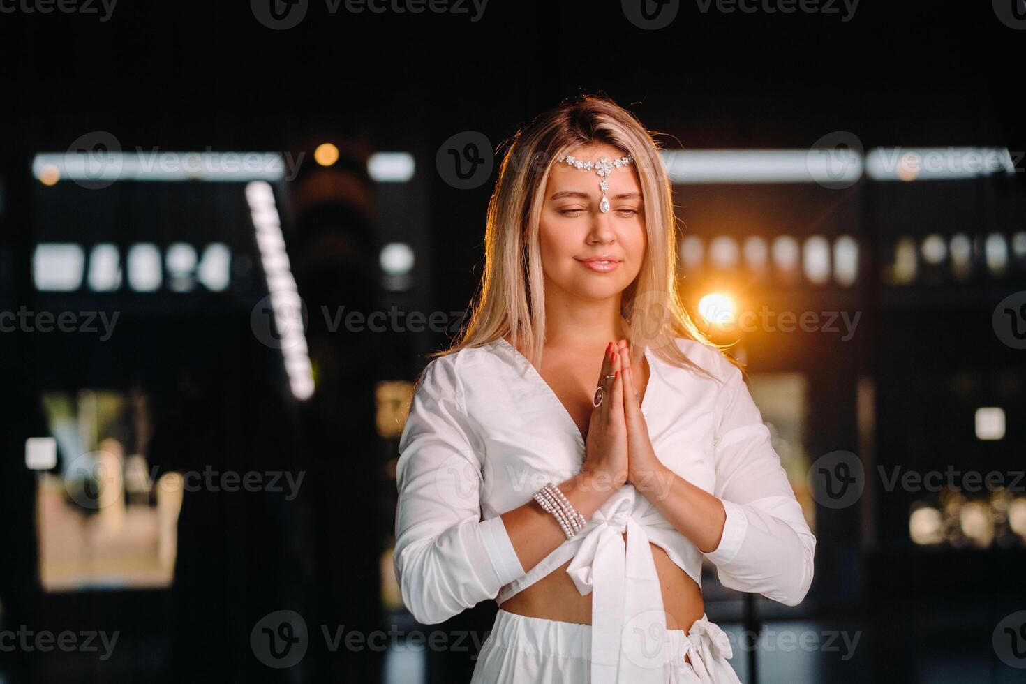 Portrait of a smiling girl in a white dress with her palms clasped in front of her photo