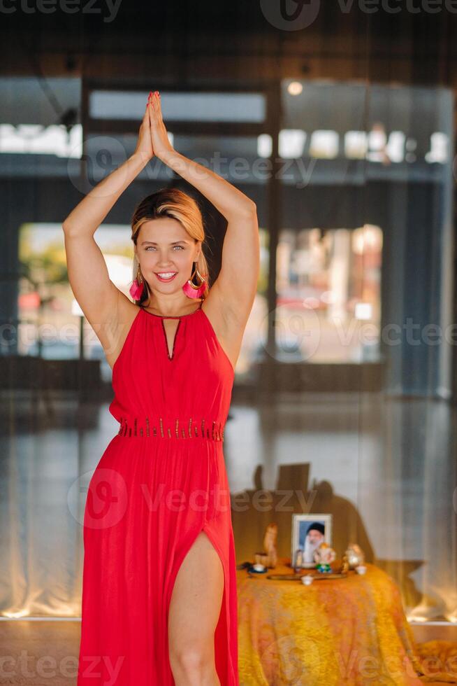 A girl in a red dress moves in a dance meditating indoors . Dynamic dance photo
