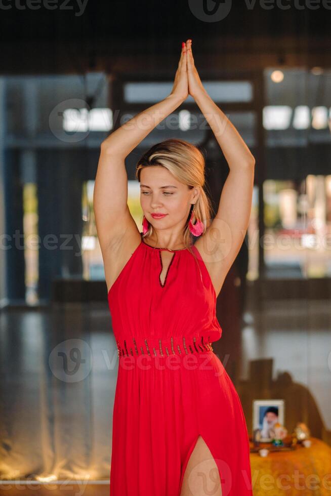 A girl in a red dress moves in a dance meditating indoors . Dynamic dance photo