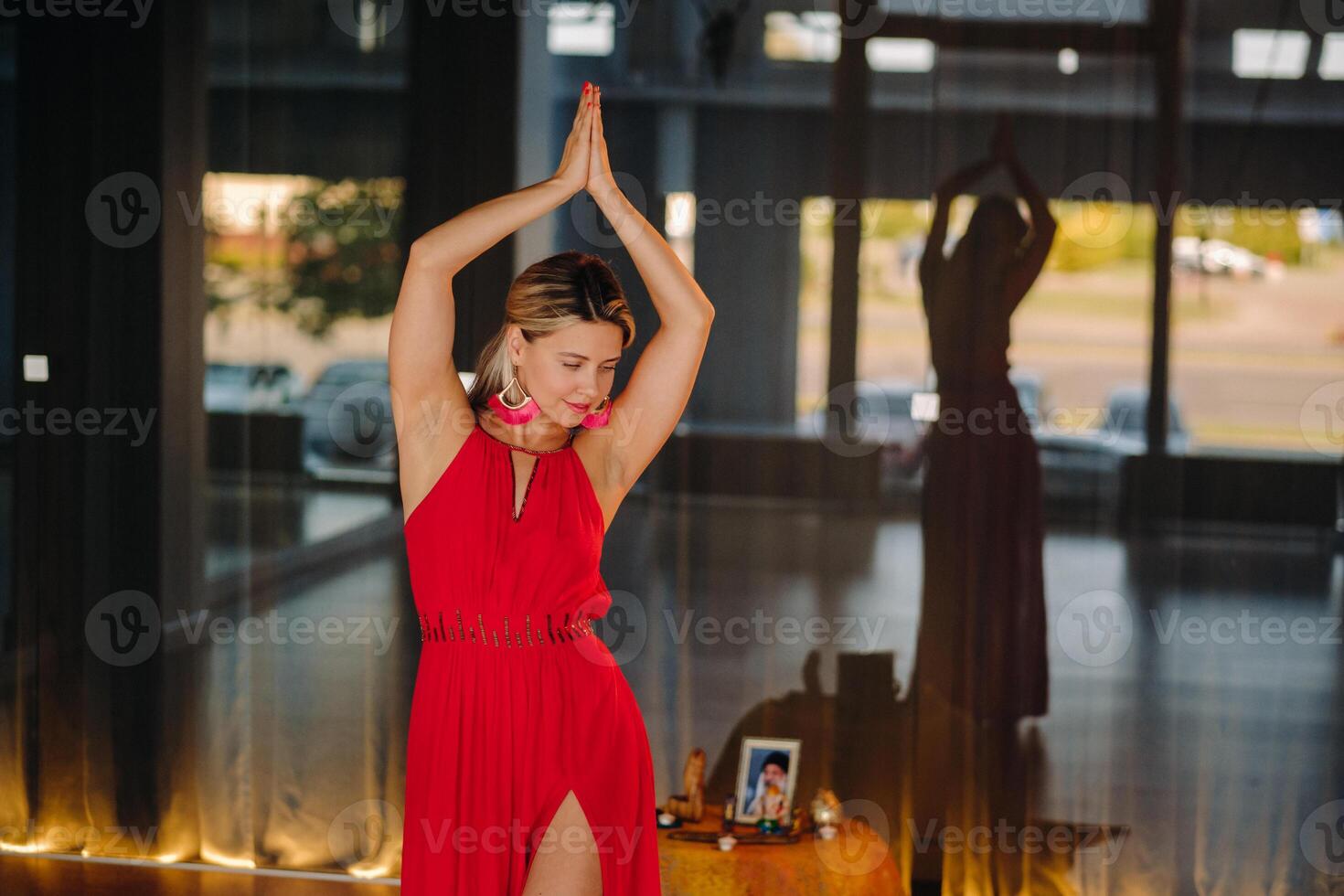 A girl in a red dress moves in a dance meditating indoors . Dynamic dance photo