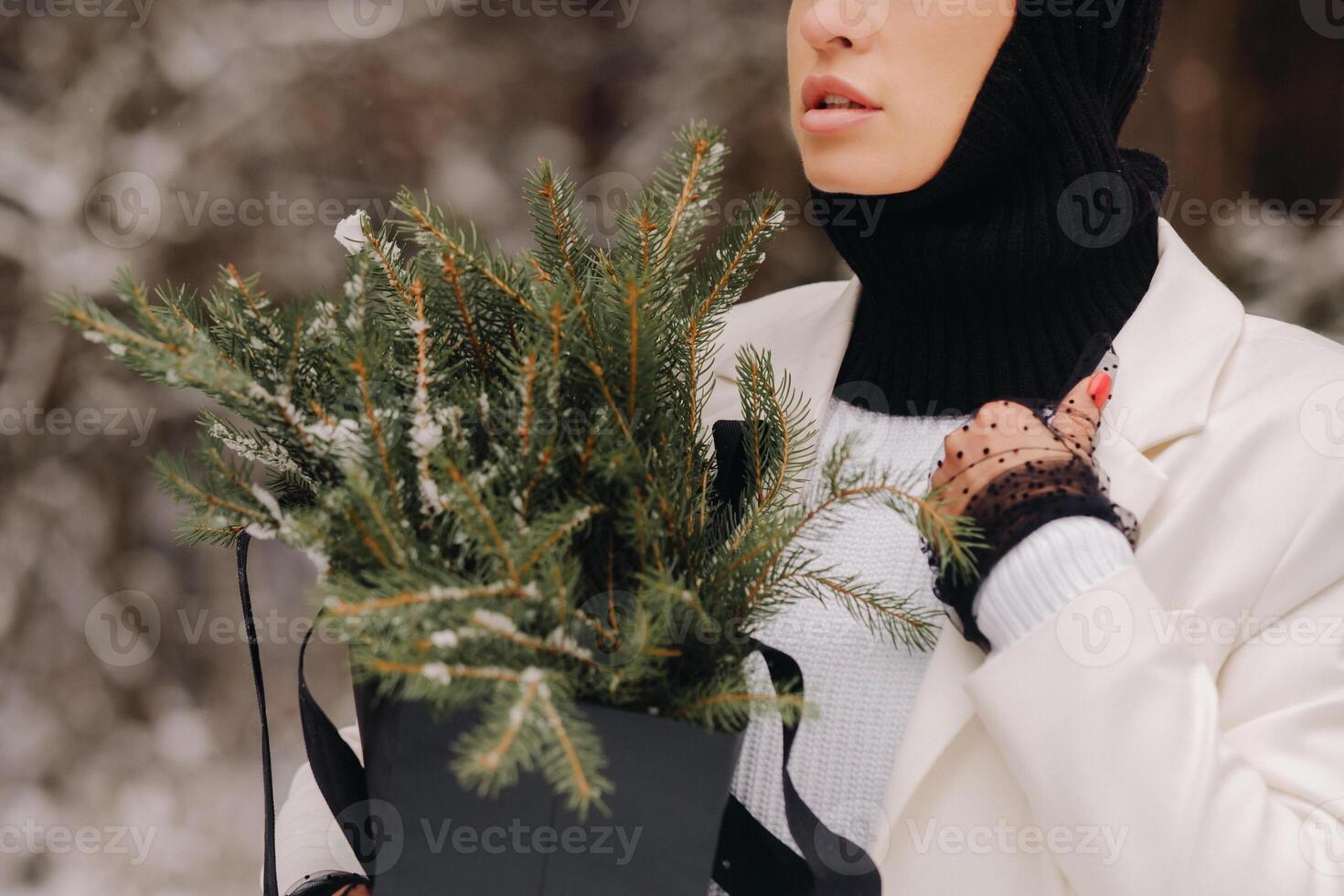 A girl in a white suit and balaclava with a package of Christmas trees in the winter forest on New Year's Eve.New Year's concept photo