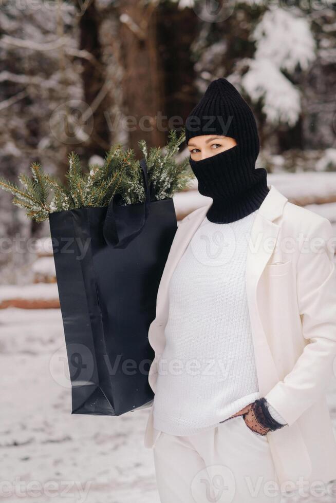 A girl in a white suit and balaclava with a package of Christmas trees in the winter forest on New Year's Eve.New Year's concept photo