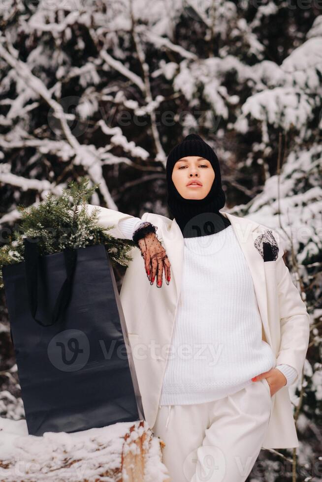 A girl in a white suit and balaclava with a package of Christmas trees in the winter forest on New Year's Eve.New Year's concept photo