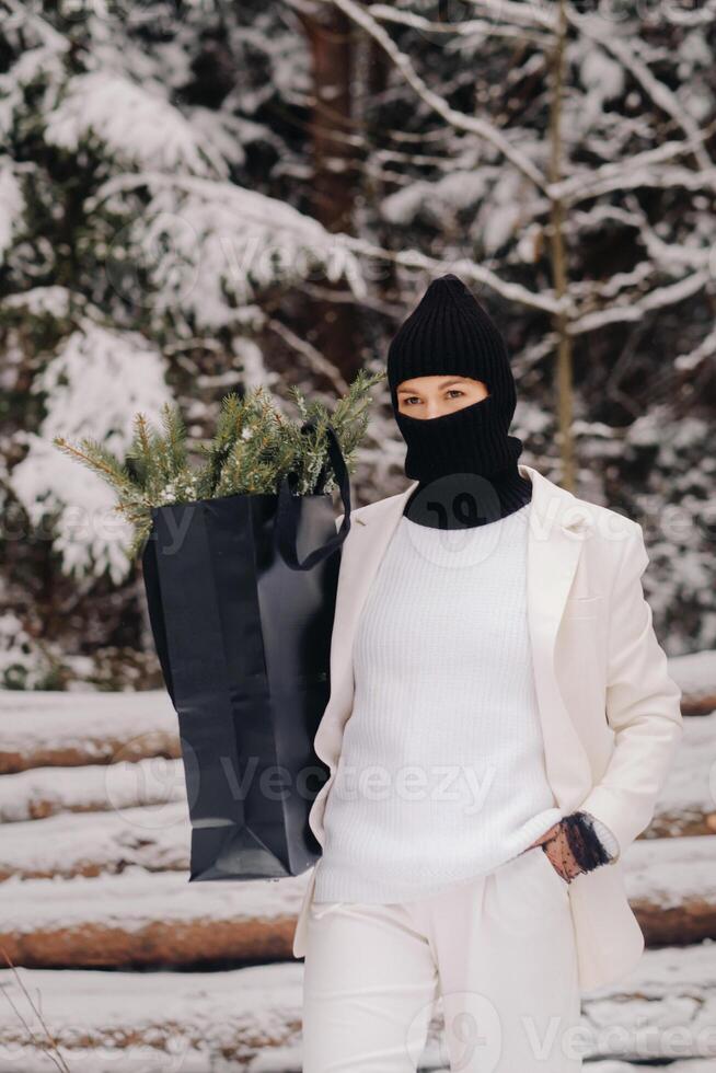 A girl in a white suit and balaclava with a package of Christmas trees in the winter forest on New Year's Eve.New Year's concept photo