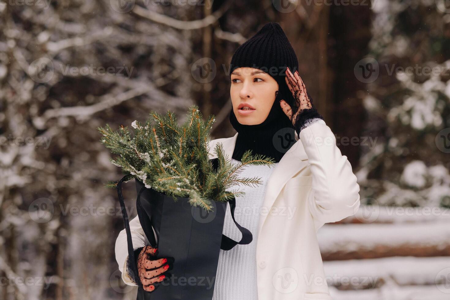 A girl in a white suit and balaclava with a package of Christmas trees in the winter forest on New Year's Eve.New Year's concept photo