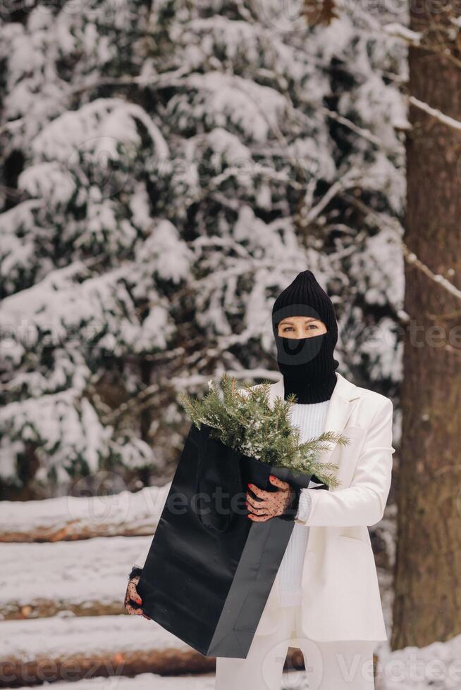 A girl in a white suit and balaclava with a package of Christmas trees in the winter forest on New Year's Eve.New Year's concept photo