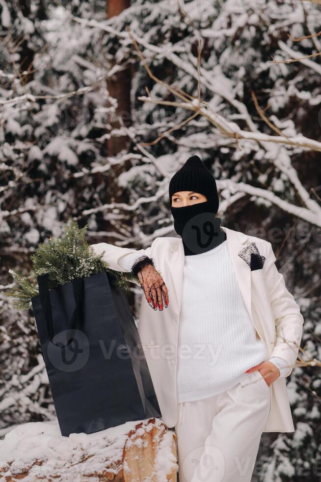 A girl in a white suit and balaclava with a package of Christmas trees in the winter forest on New Year's Eve.New Year's concept photo