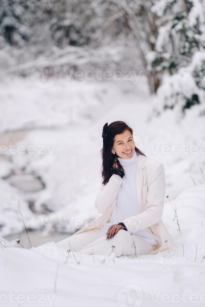 Portrait of a stylish woman in a white suit with elegant gloves sitting in nature in winter photo