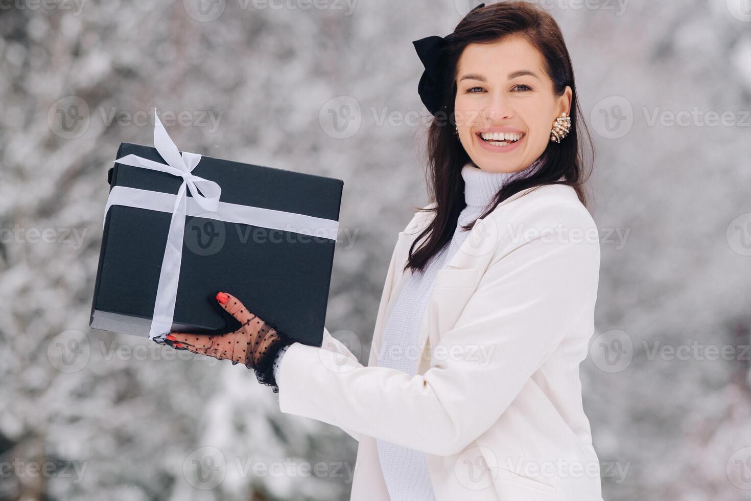 A stylish woman with a white suit with a New Year's gift in her hands in a winter forest. A girl in nature in a snowy forest with a gift box photo