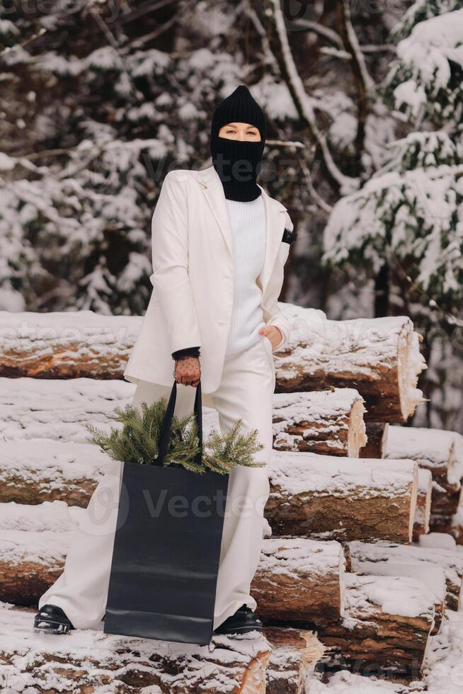 A girl in a white suit and balaclava with a package of Christmas trees in the winter forest on New Year's Eve.New Year's concept photo