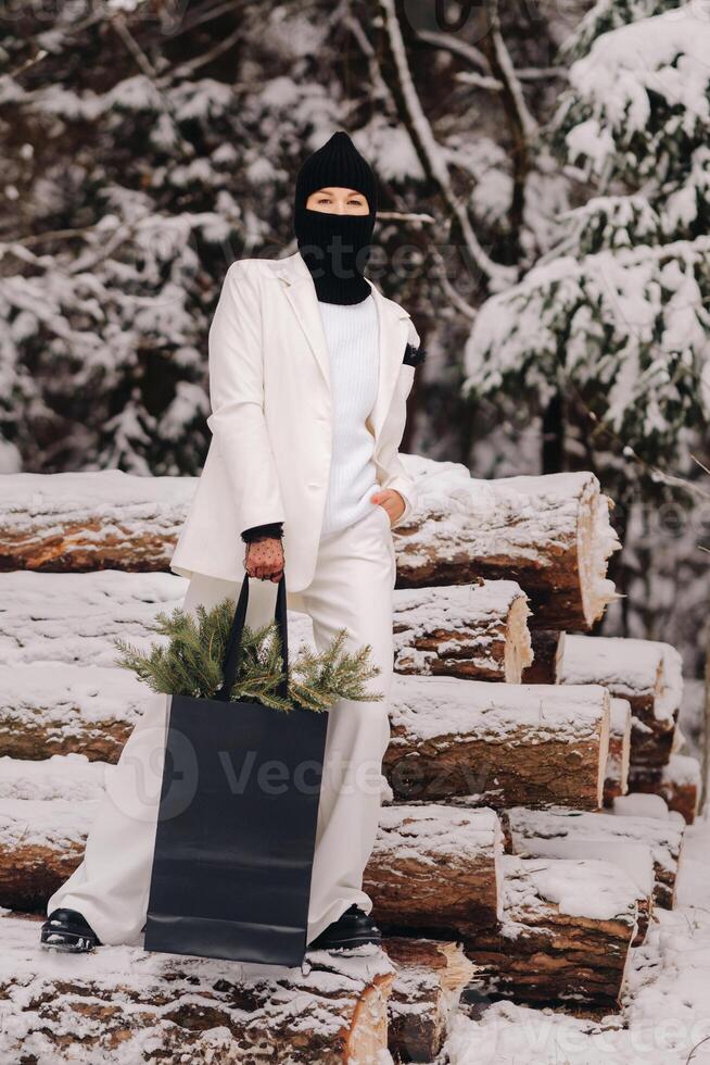 A girl in a white suit and balaclava with a package of Christmas trees in the winter forest on New Year's Eve.New Year's concept photo