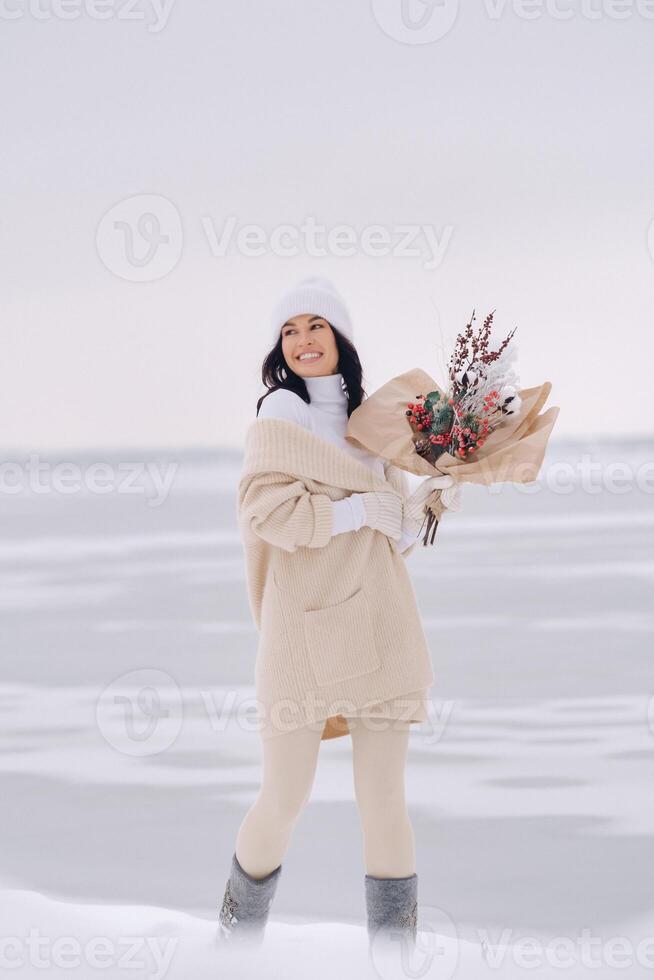 A girl in a beige cardigan and winter flowers walks in nature in the snowy season. Winter weather photo