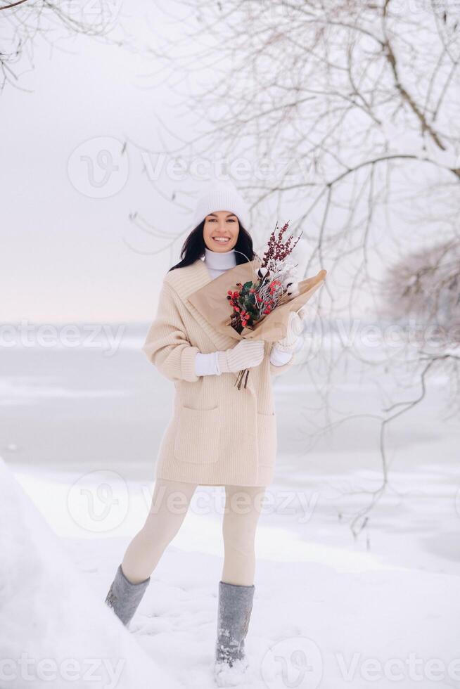 A girl in a beige cardigan and winter flowers walks in nature in the snowy season. Winter weather photo