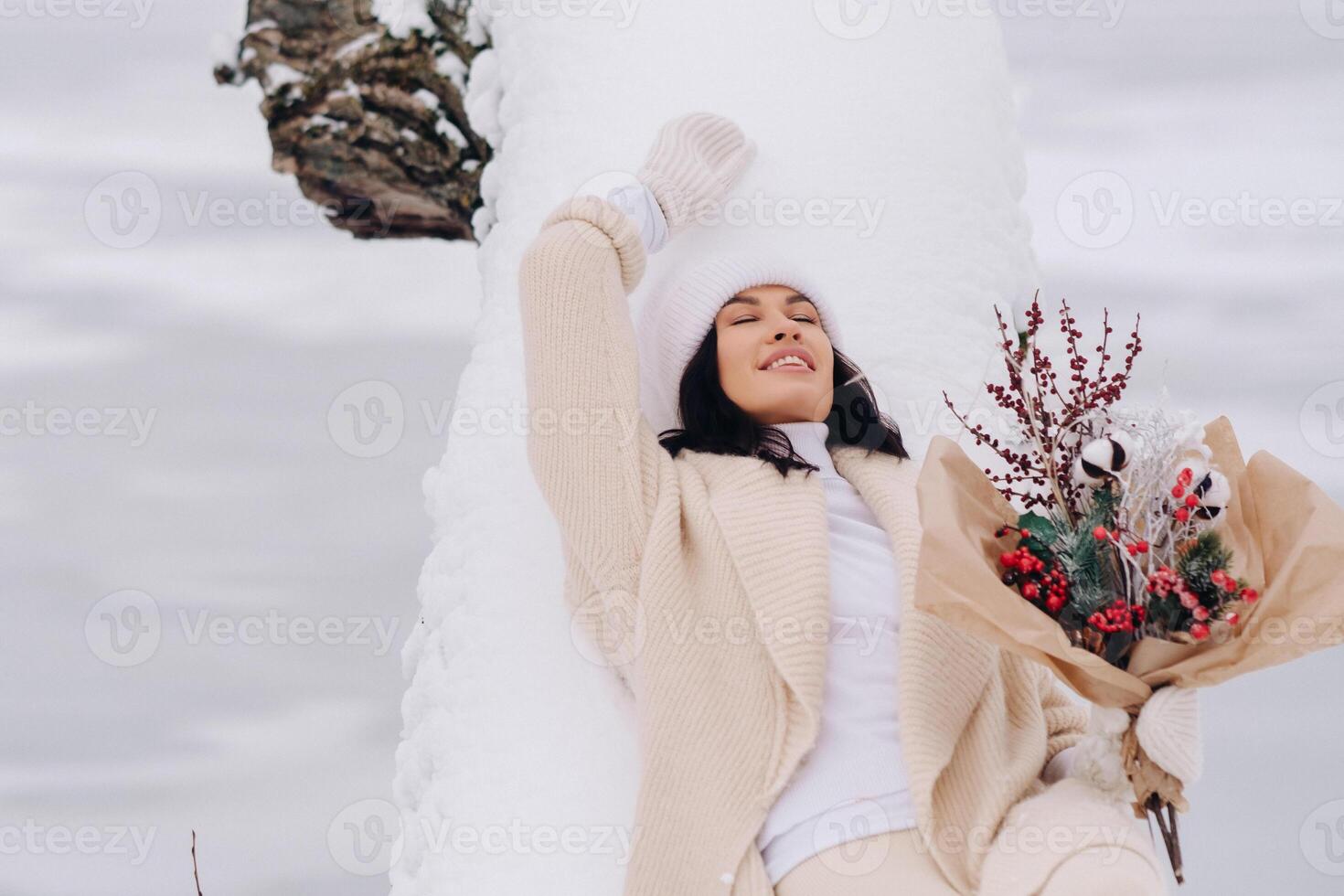 A beautiful girl in a beige cardigan and a white hat with flowers enjoys a snowy winter in nature photo