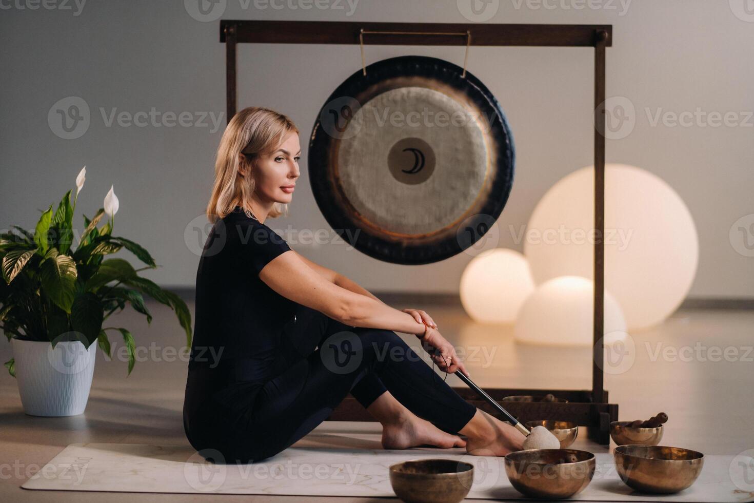 A woman sits with a hammer and next to a gong and Tibetan bowls in the interior photo