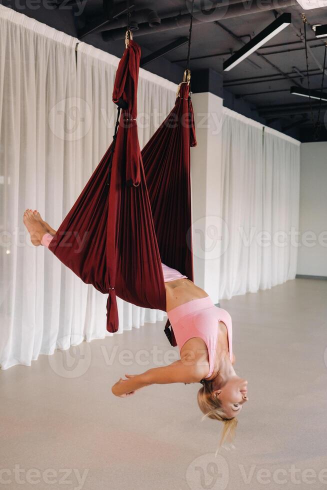A young girl, an aero yoga coach, is hanging on a hammock in the yoga club hall. a woman in pink sportswear is doing anti-gravity yoga photo