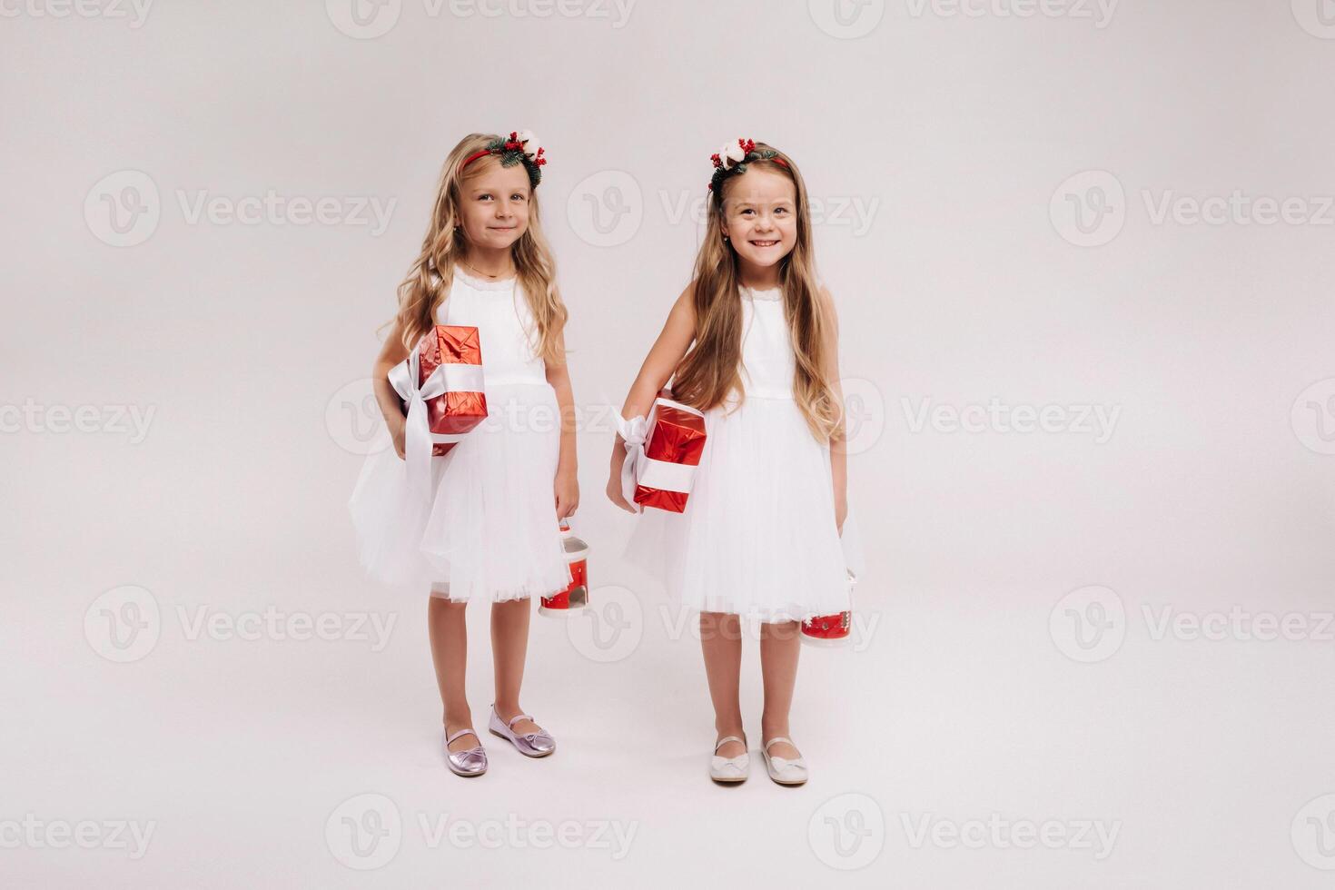 two little girls in white dresses with Christmas gifts on a white background smile photo