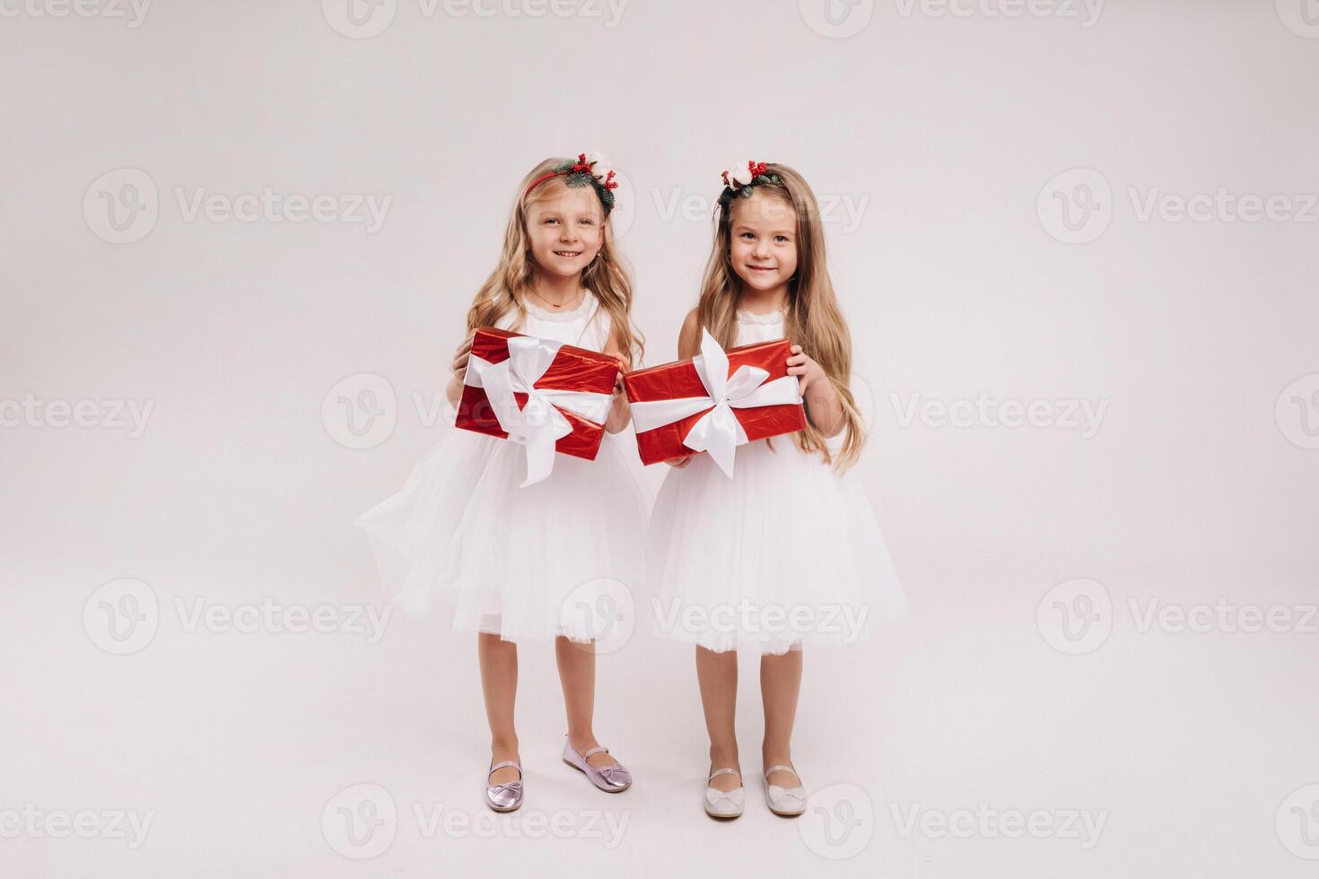 two little girls in white dresses with Christmas gifts on a white background smile photo