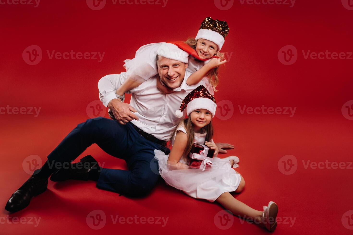 Portrait of a happy family in a Christmas hat on a red background. Dad and daughters at Christmas photo