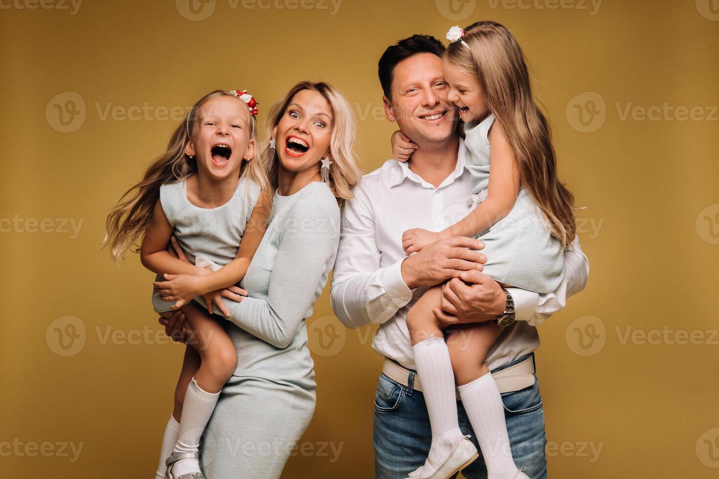 Happy parents hold their children in their arms and smile on a yellow background. an emotional family of four photo