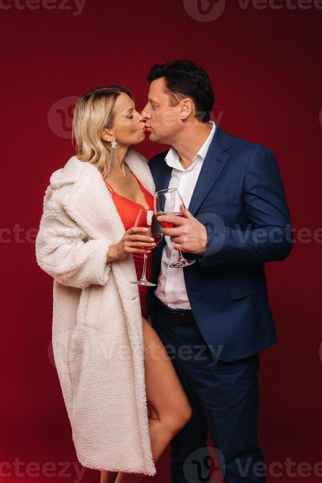 A man and a woman in love with a glass of champagne on a red background kiss photo
