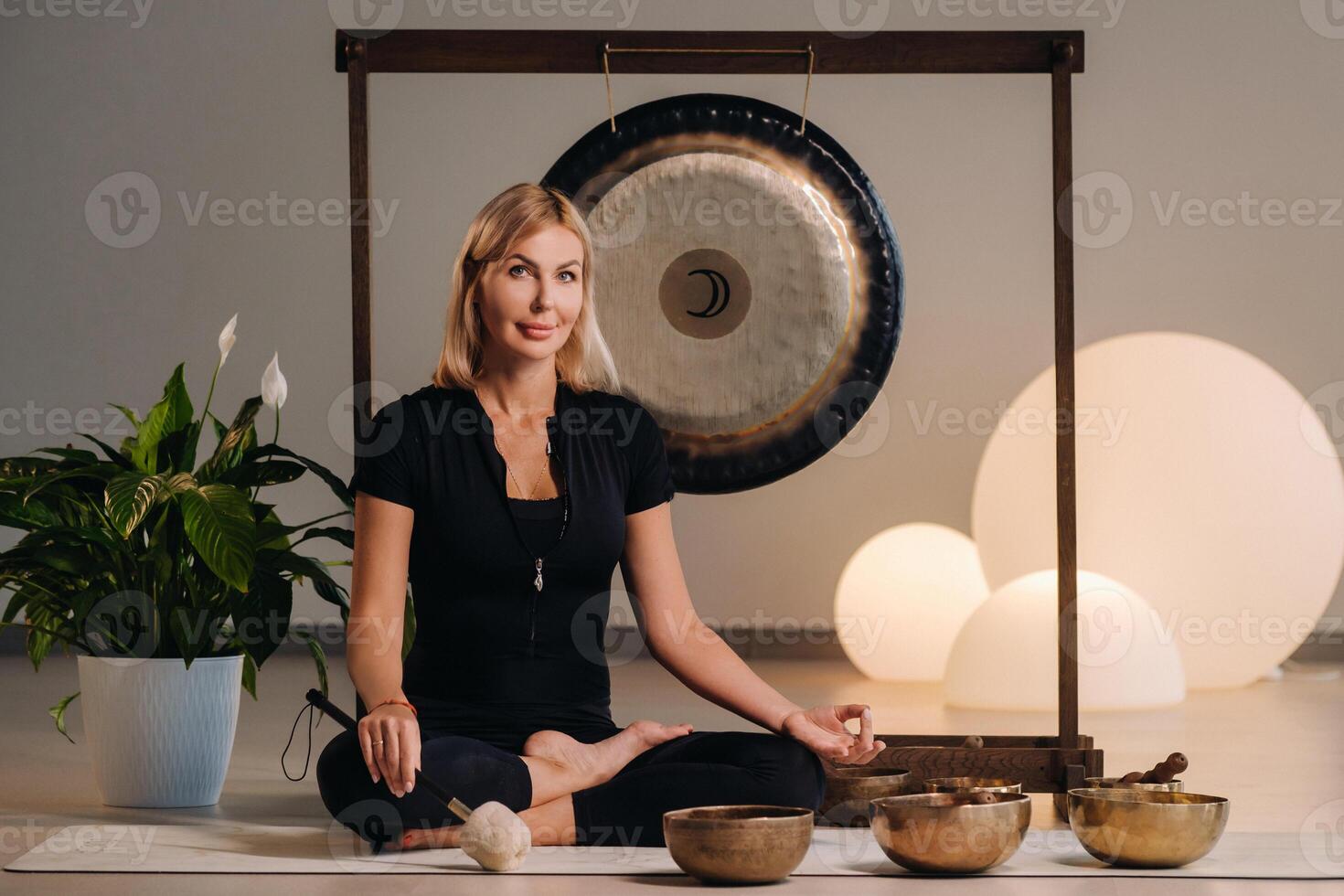 A woman sits with a hammer and next to a gong and Tibetan bowls in the interior photo