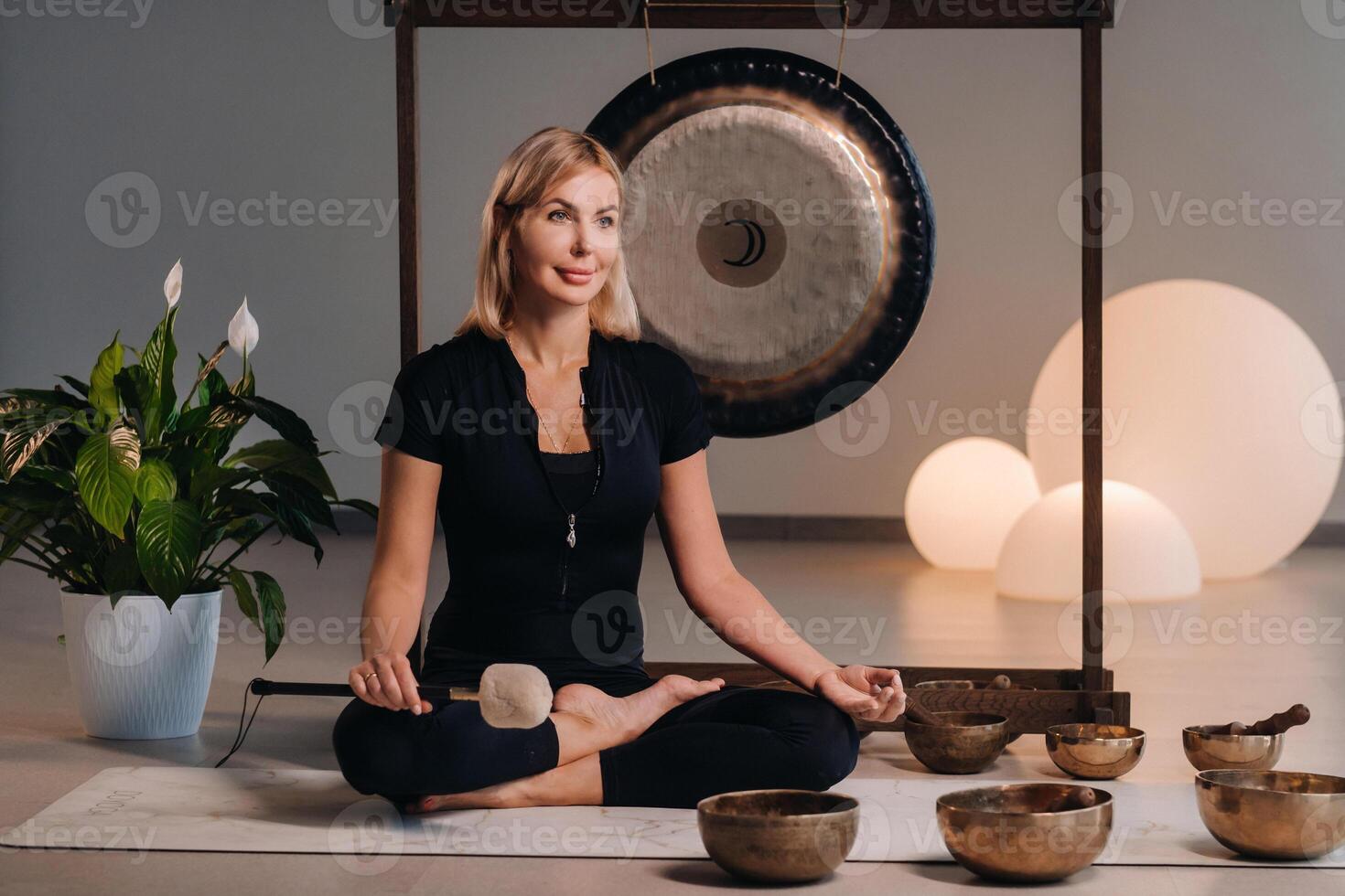 A woman sits with a hammer and next to a gong and Tibetan bowls in the interior photo