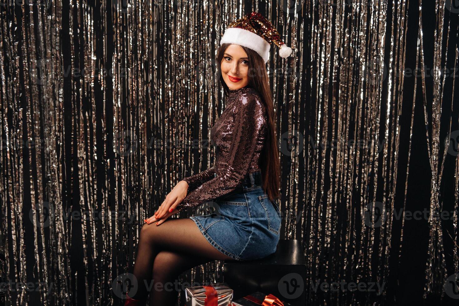 a girl in a shiny jacket with a Santa hat with gifts on a silver background in the form of rain photo