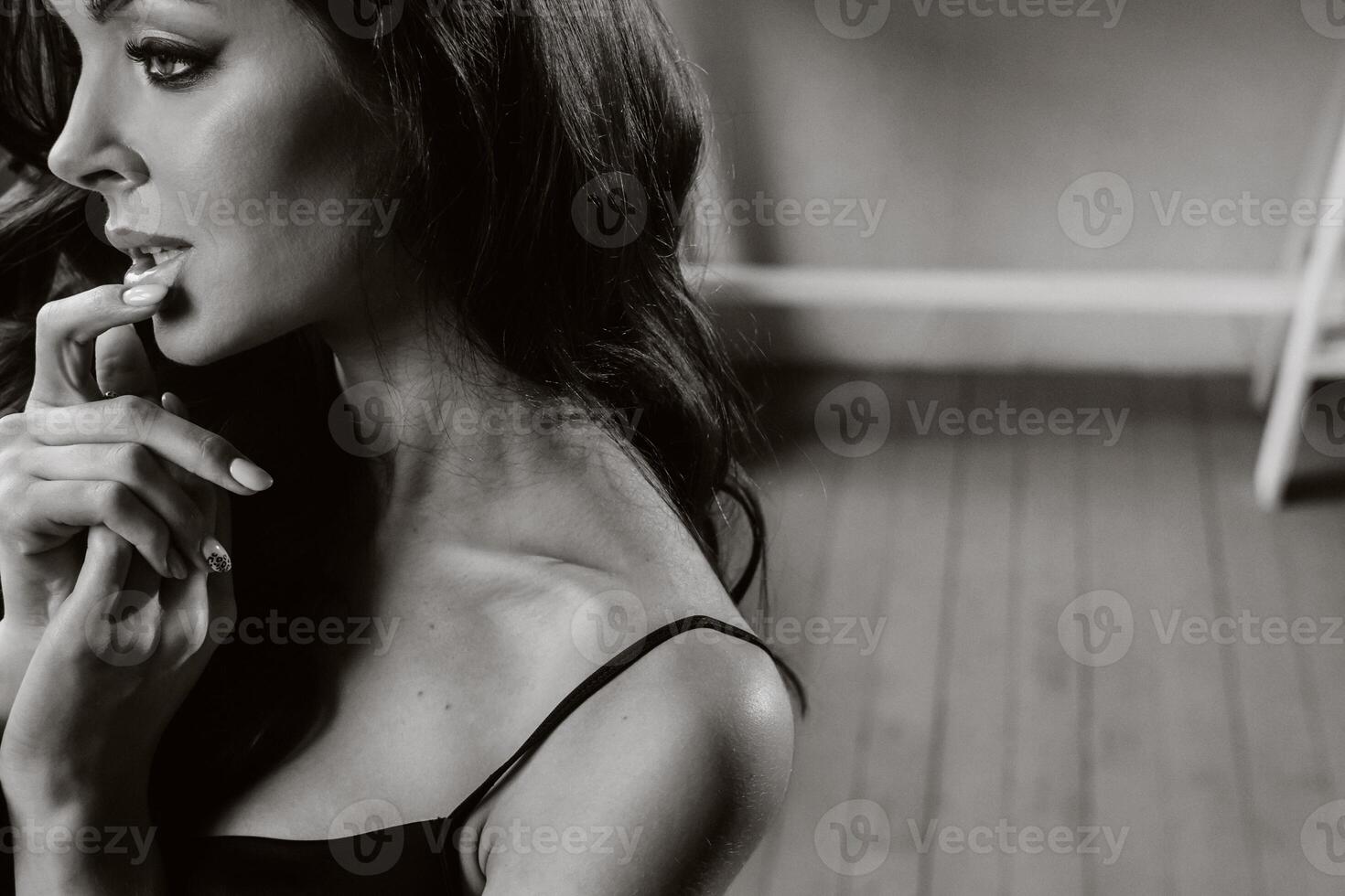 a brunette girl with long hair poses in a studio sitting on a chair.Black and white photo
