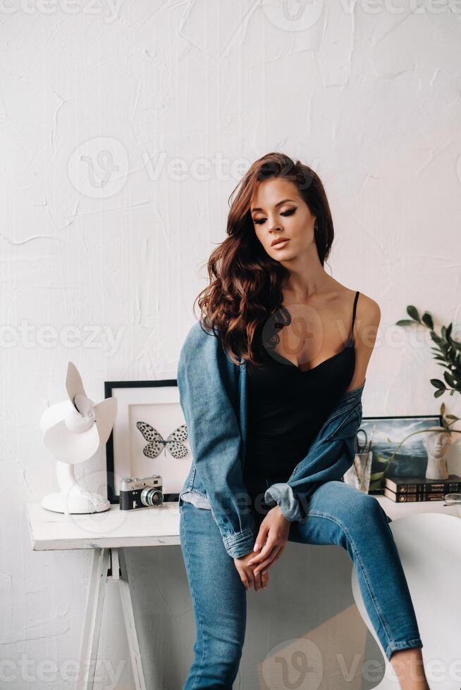 a brunette with long hair poses in the interior sitting on a table photo