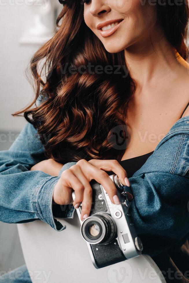 a brunette with long hair poses in a studio sitting on a chair with a camera in her hands photo