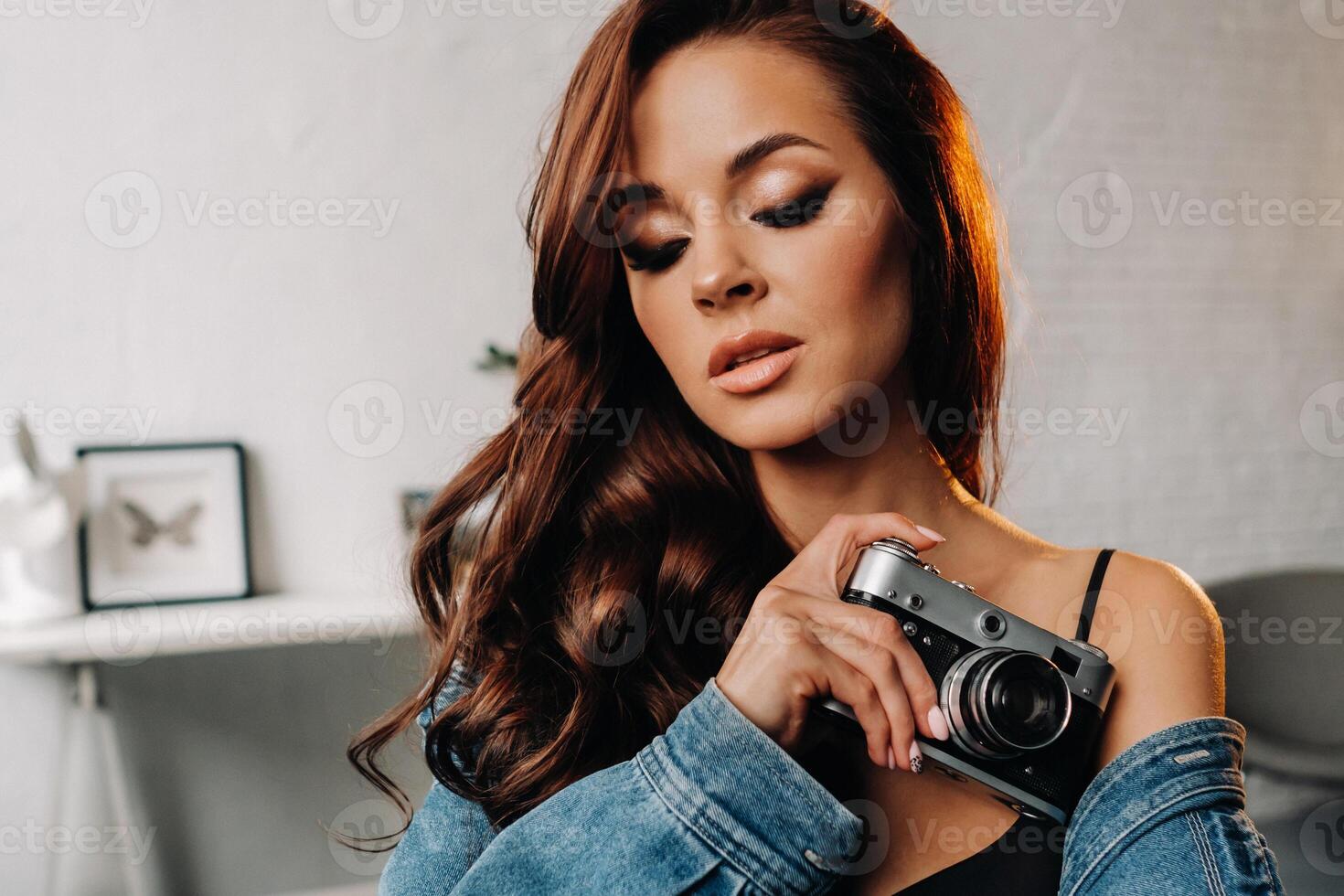 a brunette with long hair poses in a studio sitting on a chair with a camera in her hands photo