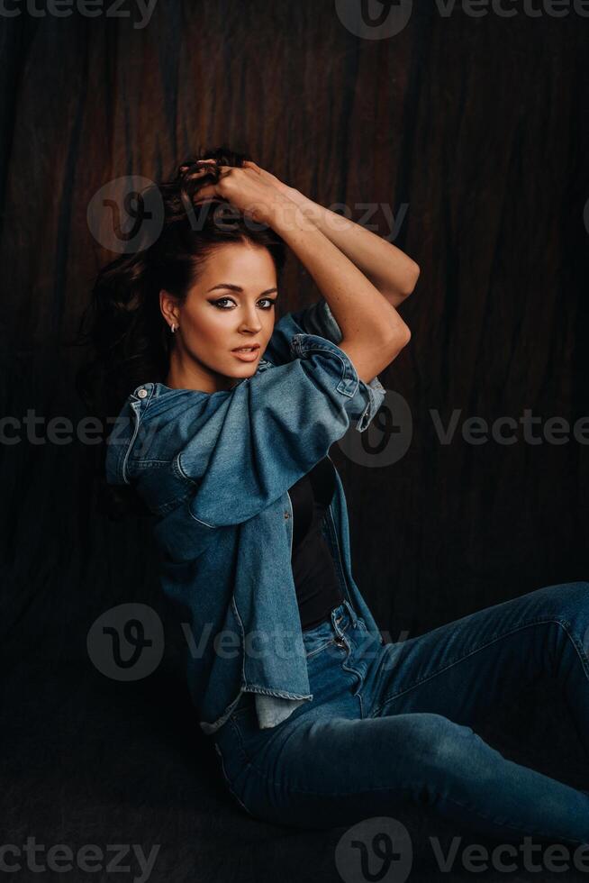 a brunette with long hair poses in a studio sitting on the floor on a black background photo