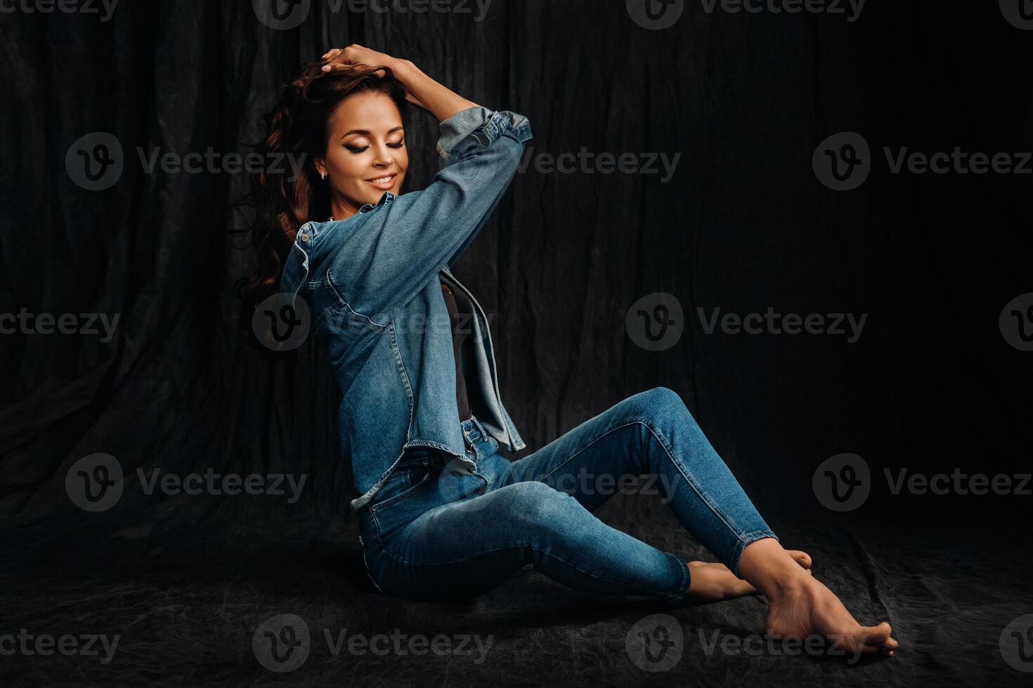 a brunette with long hair poses in a studio sitting on the floor on a black background photo