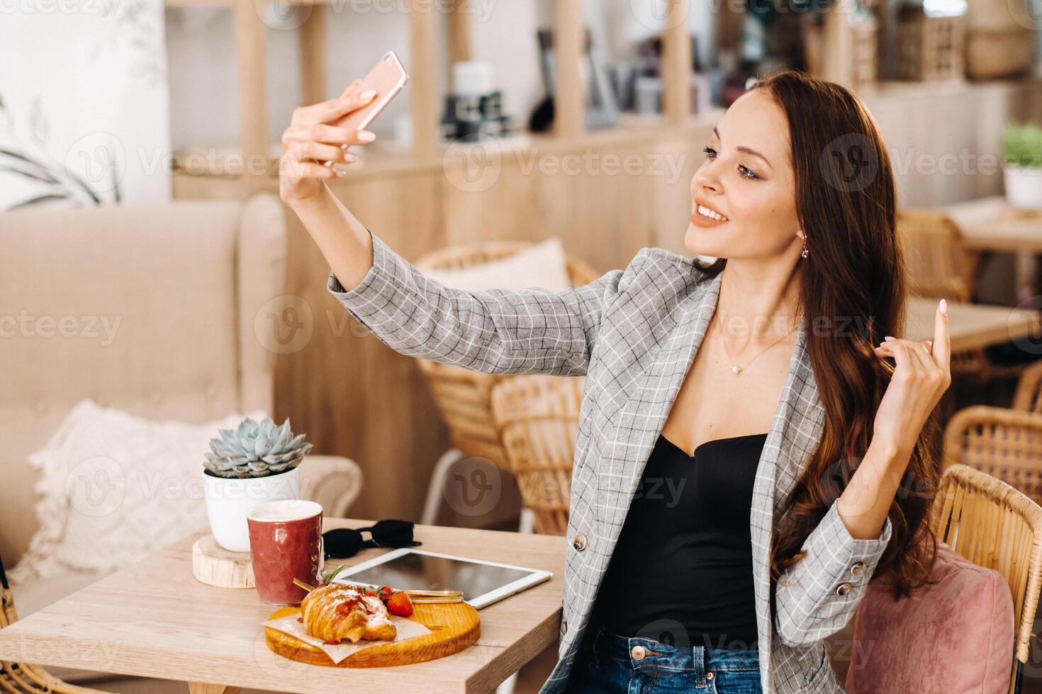 a business Girl is sitting in a cafe and taking a selfie,a Girl in a coffee shop is smiling and taking a selfie on a smartphone photo