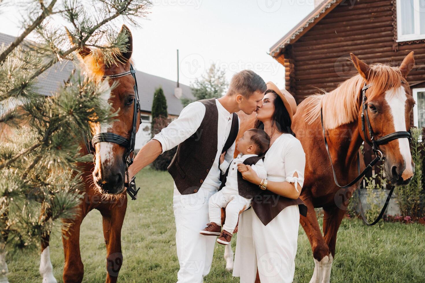 A family in white clothes with their son stand near two beautiful horses in nature. A stylish couple with a child are photographed with horses photo