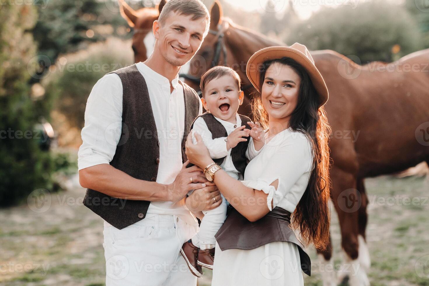 A family in white clothes with their son stand near two beautiful horses in nature. A stylish couple with a child are photographed with horses photo