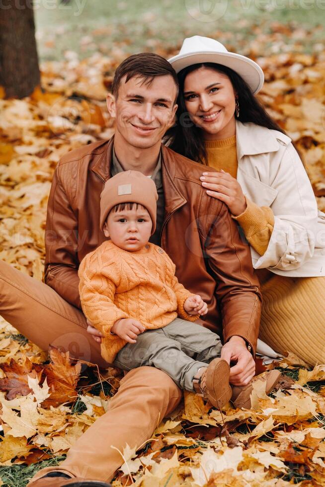 Father and mother with son sitting in the autumn Park. Portrait of a Golden autumn Family in a nature Park. photo