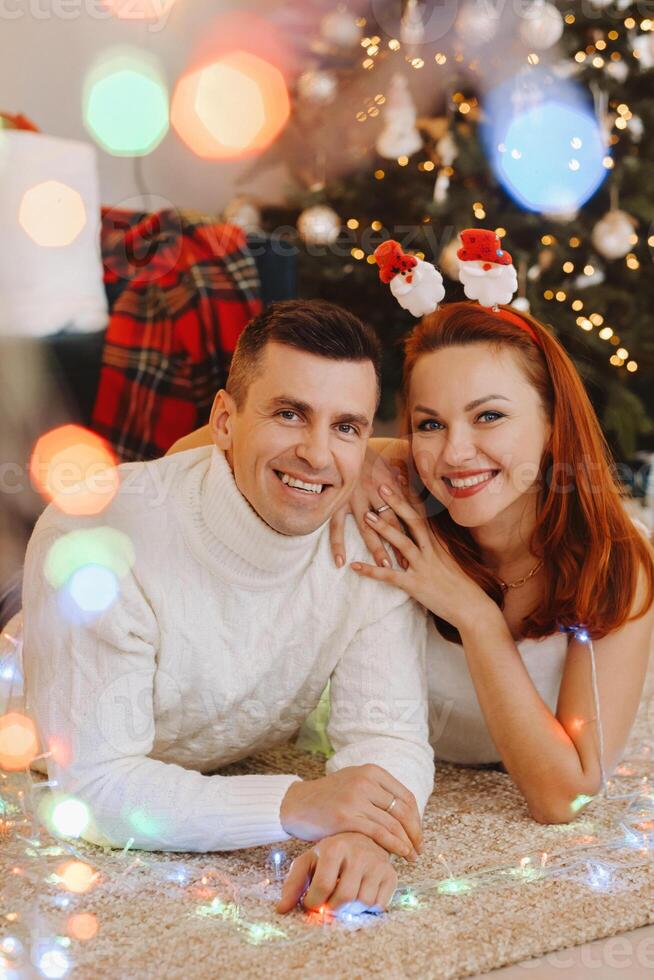 a happy married couple is lying on the floor near the Christmas tree at home photo