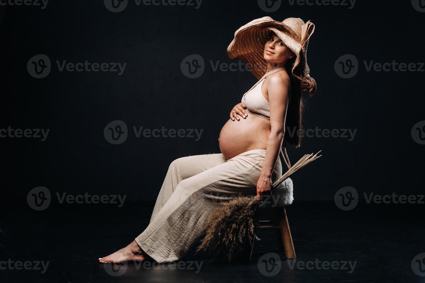 pregnant woman in a straw hat with beige clothes with a bouquet in her hands in the studio on a black background photo
