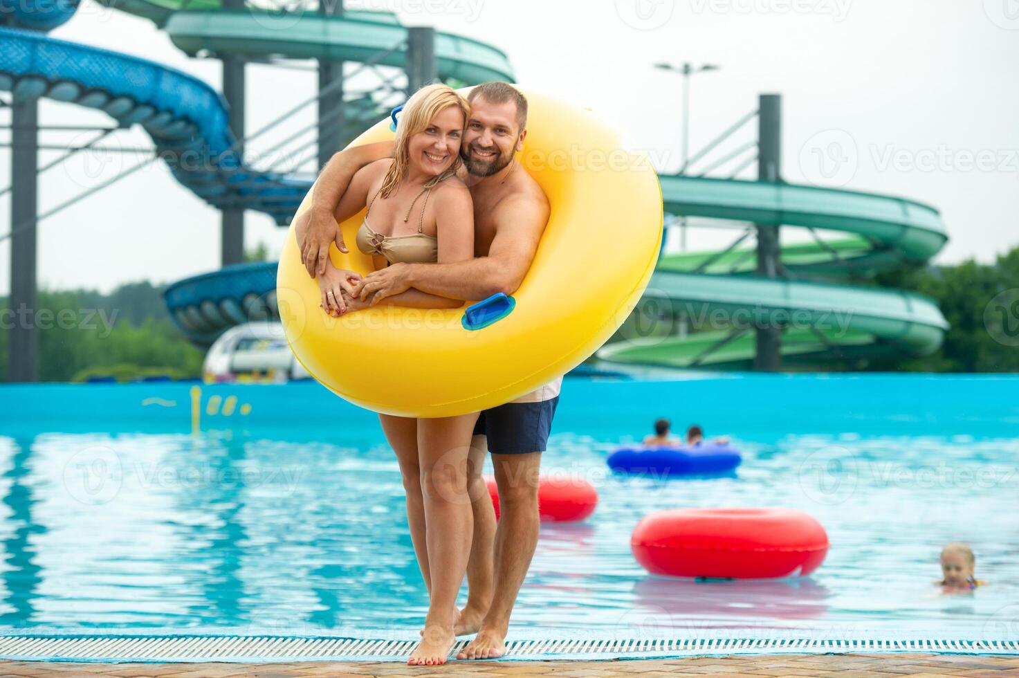 a man and a woman in a rubber inflatable circle stand against the background of a summer water park pool photo