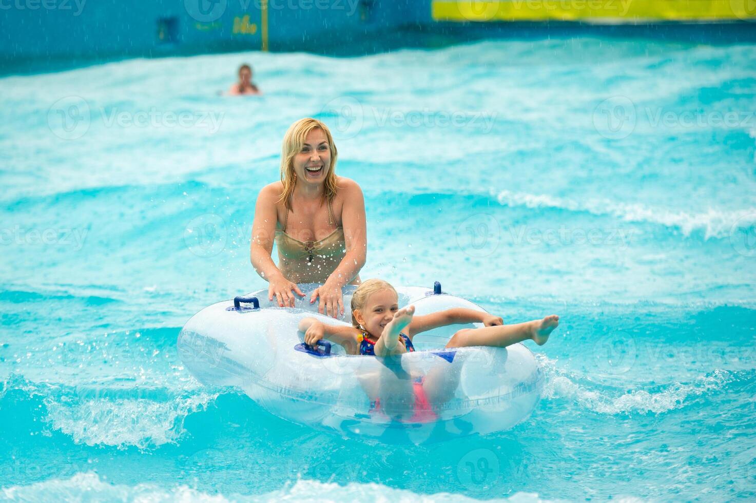 a woman with a child in a rubber inflatable circle plays in the pool of a summer water park in the rain photo