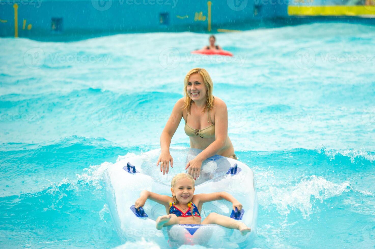 a woman with a child in a rubber inflatable circle plays in the pool of a summer water park in the rain photo