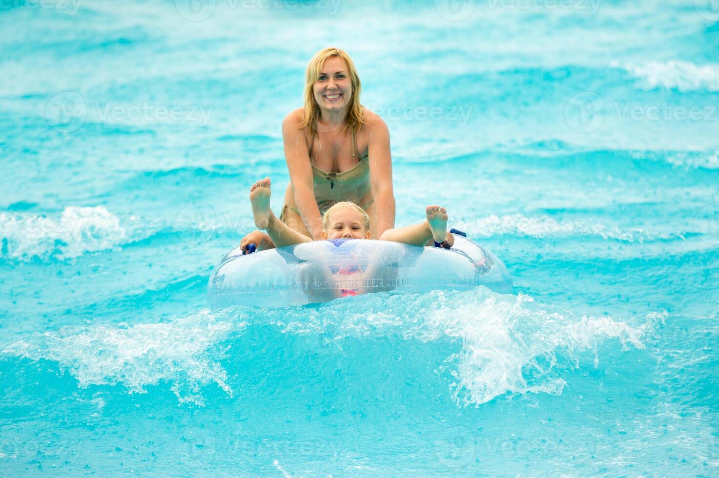 a woman with a child in a rubber inflatable circle plays in the pool of a summer water park in the rain photo