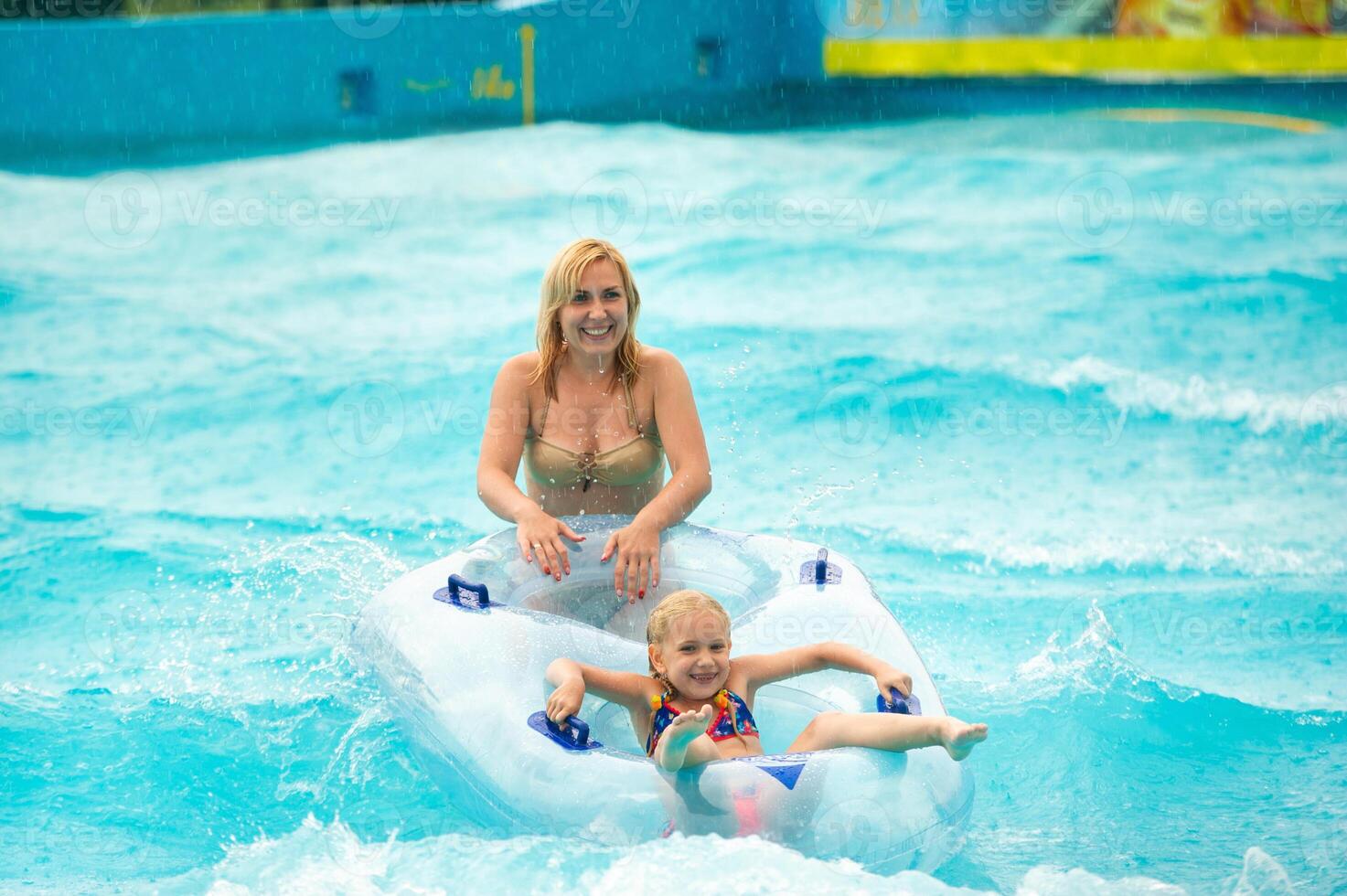 a woman with a child in a rubber inflatable circle plays in the pool of a summer water park in the rain photo