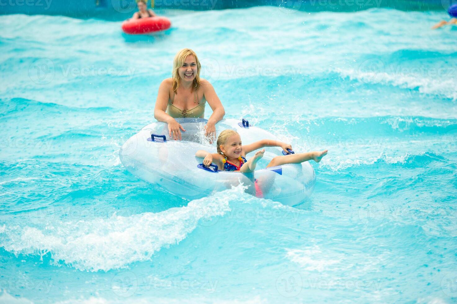 a woman with a child in a rubber inflatable circle plays in the pool of a summer water park in the rain photo